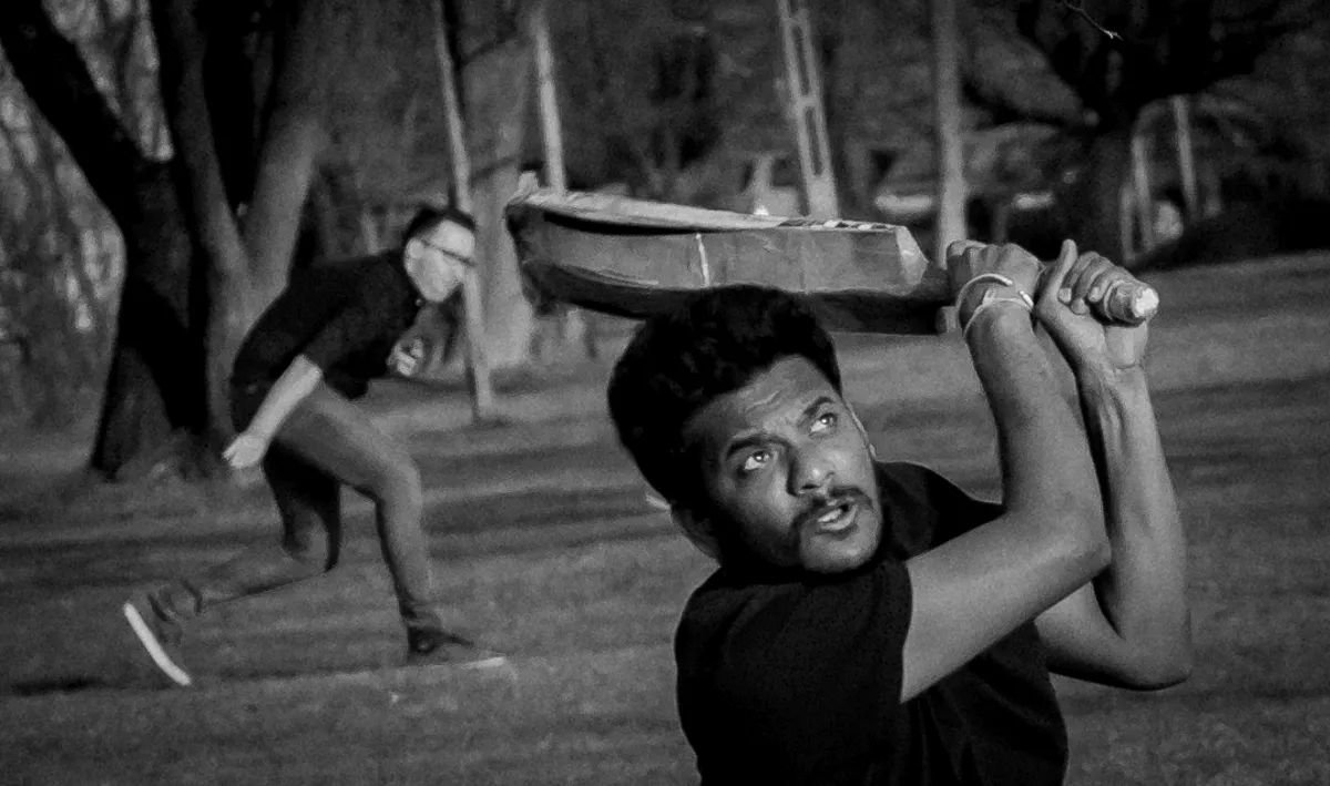 Young man swinging a flat board overhead while another runner blurs behind him
